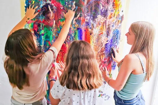 Kinder malen mit ihren Händen an einem bunten Papier, das an der Wand hängt.